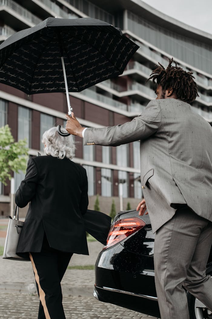 Two business professionals with an umbrella near a élégant car in an urban setting.